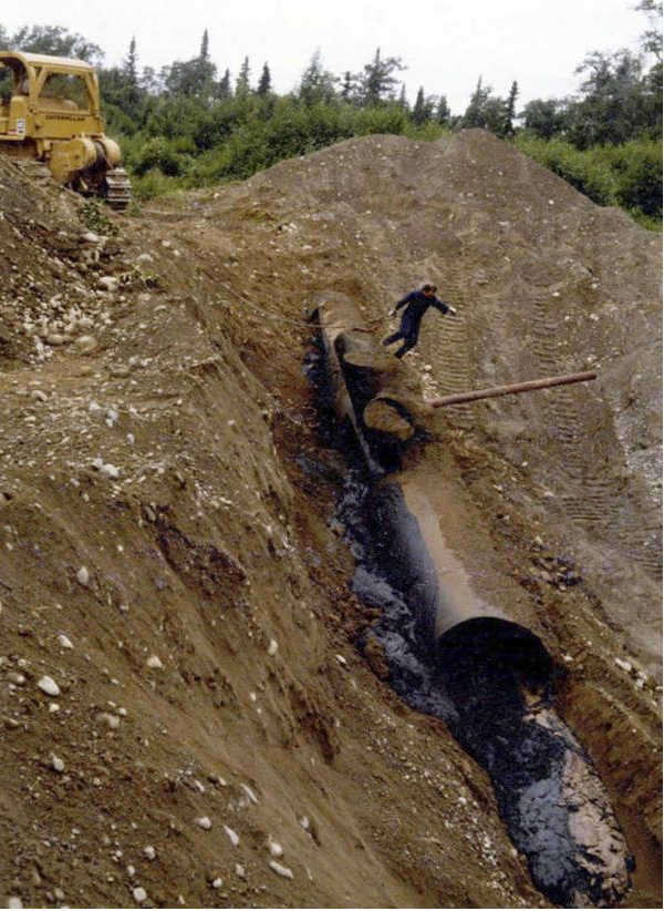 Alaska Department of Environmental Conservation file photo  An Alaska Department of Environmental Conservation staff member secures a chain to an unearthed 40-foot pipe used at the Arness Septage Site. The pipe was installed on the land previous to a 1979 permit seeking to expand the facility, including a 21-tank system, to hold petroleum products, drilling muds and other sludge. That permit was not approved, but in the late 1980s, DEC excavated more than 4,200 gallons of oily waste at the site in addition to hundreds of barrels containing various oil industry wastes.