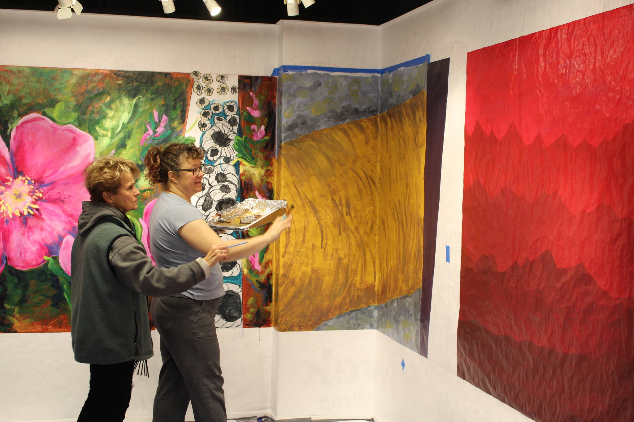 Peninsula Art Guild Vice President Marion Nelson, left, and artist Rachel Grossl examine a portion of the “Gather” mural at the Kenai Fine Art Center in Kenai, Alaska, on Saturday, Nov. 2, 2019. (Photo by Brian Mazurek/Peninsula Clarion)