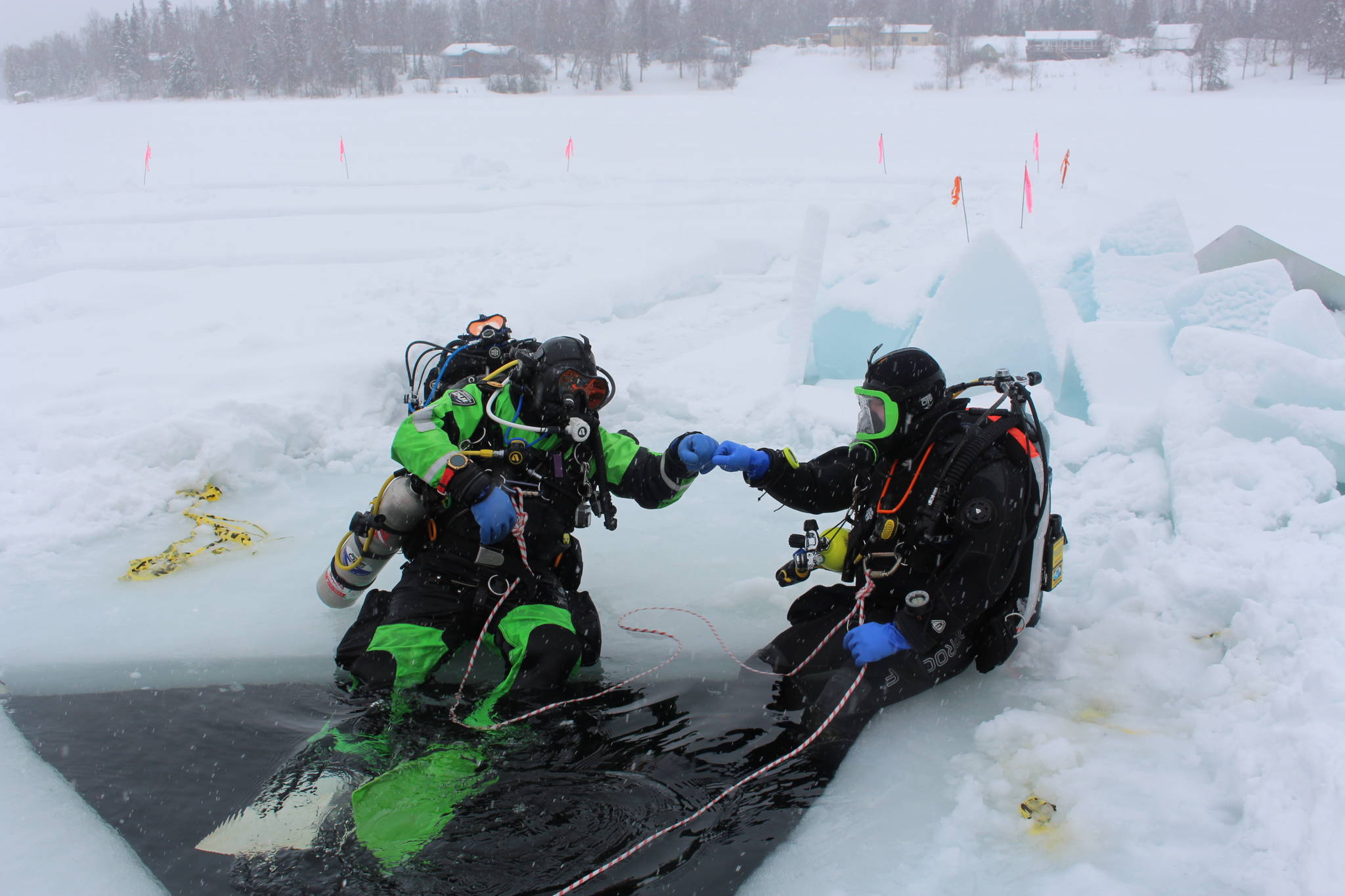 Stephen Robertson, left, and T.J. Cox, right, bump fists before diving into the icy water of Island Lake in Nikiski, Alaska on March 21, 2020. (Photo by Brian Mazurek/Peninsula Clarion)