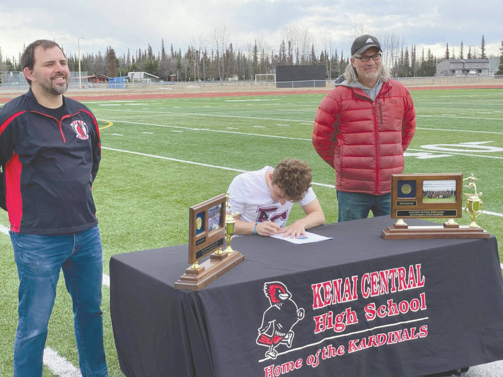 Kenai Central senior Travis Verkuilen signs to play at Earlham College in Richmond, Indiana, while head coach Shane Lopez and assistant Scott Pitsch watch Monday, May 4, 2020, at Kenai Central High School in Kenai, Alaska. (Photo provided)