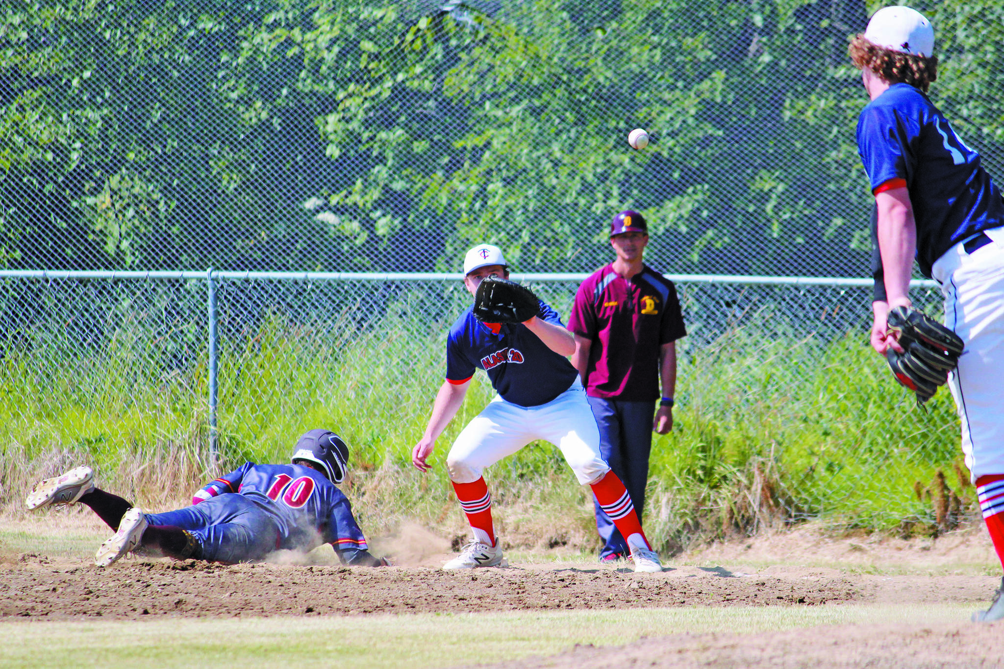 Alaska 20 pitcher Mose Hayes throws the ball to teammate Tanner Ussing while Dimond player Logan Sweet dives back onto first base during a Saturday, July 4, 2020 Alliance Baseball League game at Karen Hornaday Park in Homer, Alaska. (Photo by Megan Pacer/Homer News)