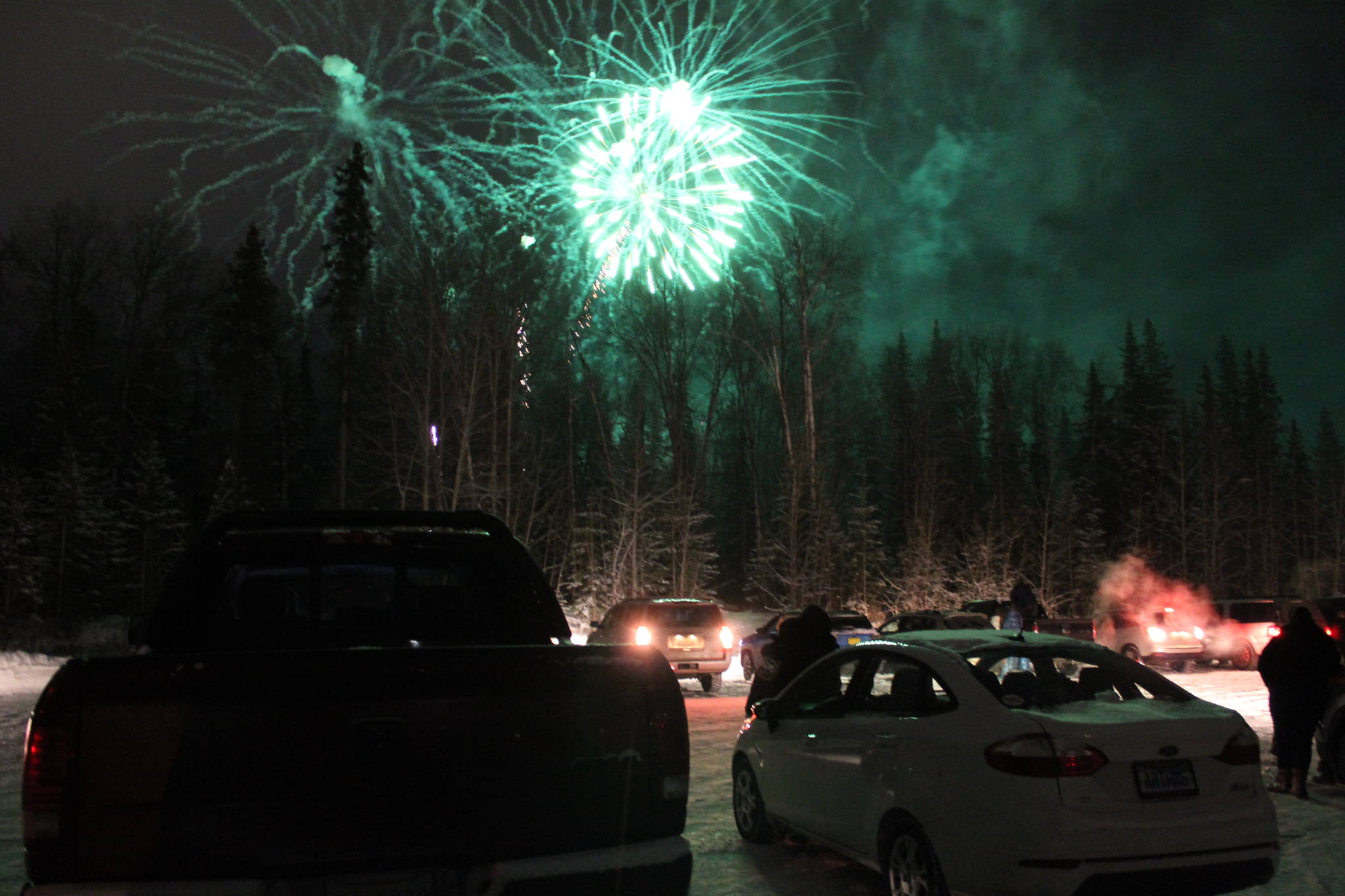 Fireworks are seen above cars at the Soldotna Regional Sports Complex on Friday, Dec. 18 in Soldotna, Alaska. (Ashlyn O’Hara/Peninsula Clarion)