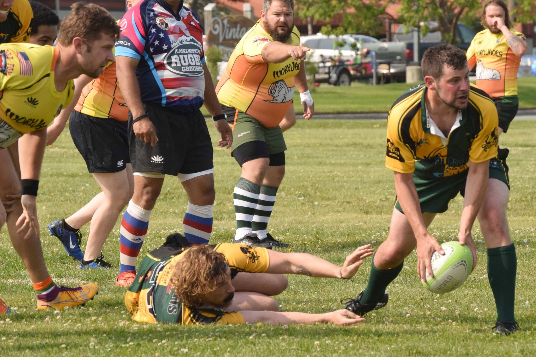 Kenai River Wolfpack scrum half Dan Balmer scoops up the ball left by tackled player Mike Curtis and passes it out to a receiving Wolfpack player while Fairbanks defenders Joshua Harold, Joe Prete and Sam Warner look on at Millennium Square in Kenai, Alaska, on Saturday, July 17, 2021, at the 2021 Kenai Dipnet Fest Rugby 10s Tournament.