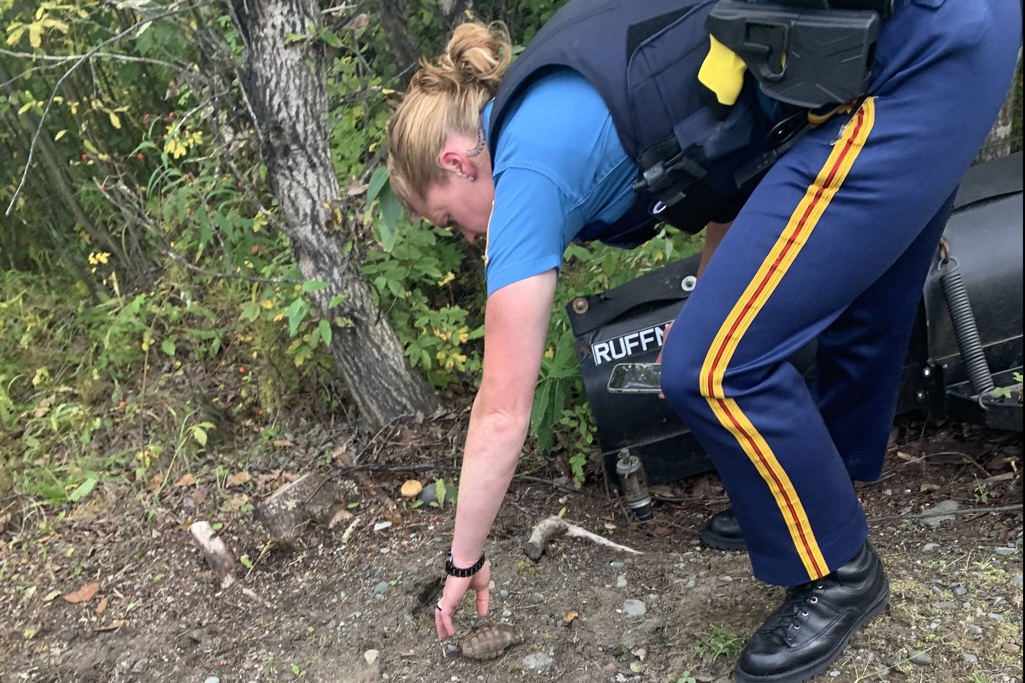 An Alaska State Trooper reaches for a grenade on Tuesday, Sept. 7, 2021 near Soldotna, Alaska. The grenade was found by 13-year-old Edith Watts on the family property in Ridgeway. Troopers and Joint Base Elmendorf-Richardson’s Explosive Ordnance Disposal Company responded to the scene. (Photo by Edith Watts)