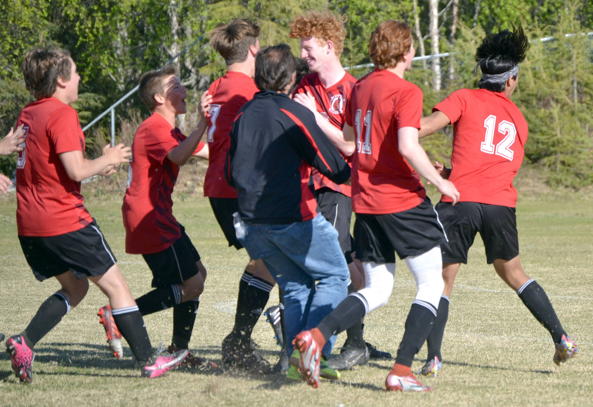 The Kenai Central boys soccer teams mobs Joe Hamilton (center) after Hamilton scored the game-winning penalty kick in the Peninsula Conference championship game Saturday, May 21, 2022, at Nikiski High School in Nikiski, Alaska. (Photo by Jeff Helminiak/Peninsula Clarion)