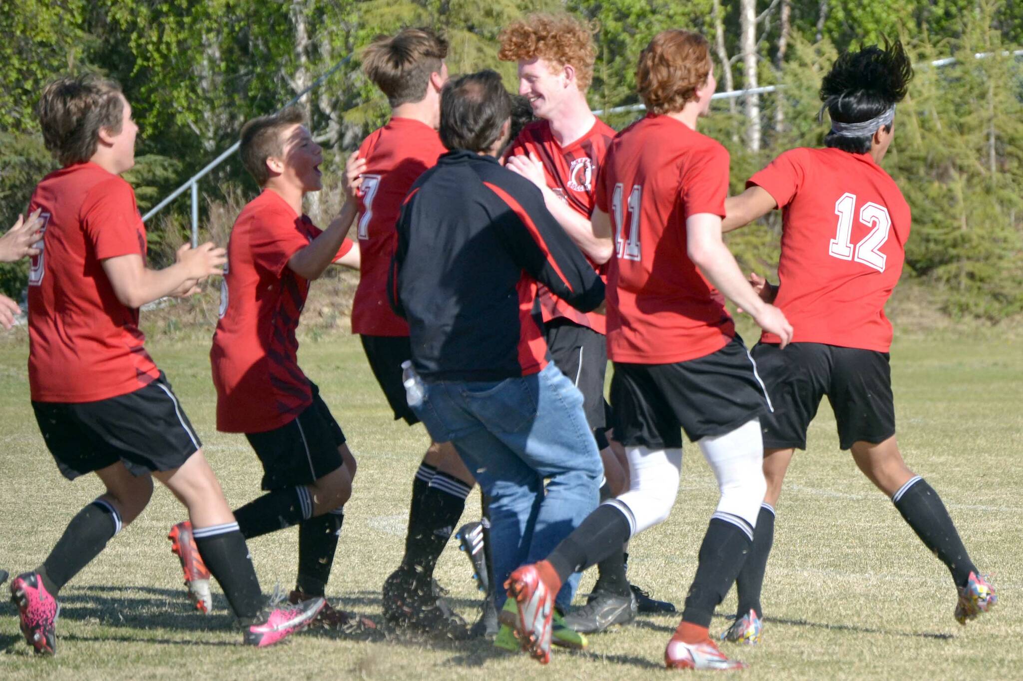 The Kenai Central boys soccer teams mobs Joe Hamilton (center) after Hamilton scored the game-winning penalty kick in the Peninsula Conference championship game Saturday, May 21, 2022, at Nikiski High School in Nikiski, Alaska. (Photo by Jeff Helminiak/Peninsula Clarion)