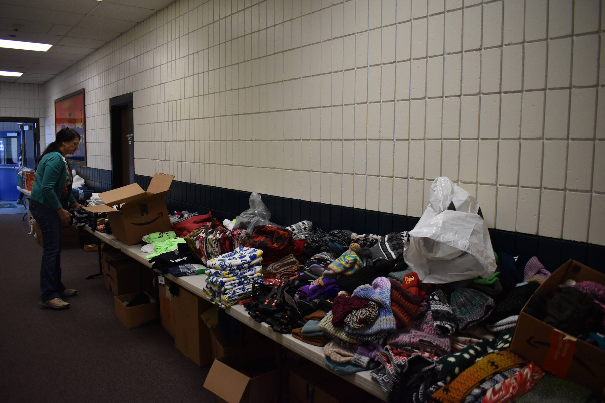 Tables are covered with piles of donated winter gear, including hats, gloves, blankets and ice cleats during Project Homeless Connect on Tuesday, Jan. 31, 2023, at the Soldotna Regional Sports Complex in Soldotna, Alaska. (Jake Dye/Peninsula Clarion)