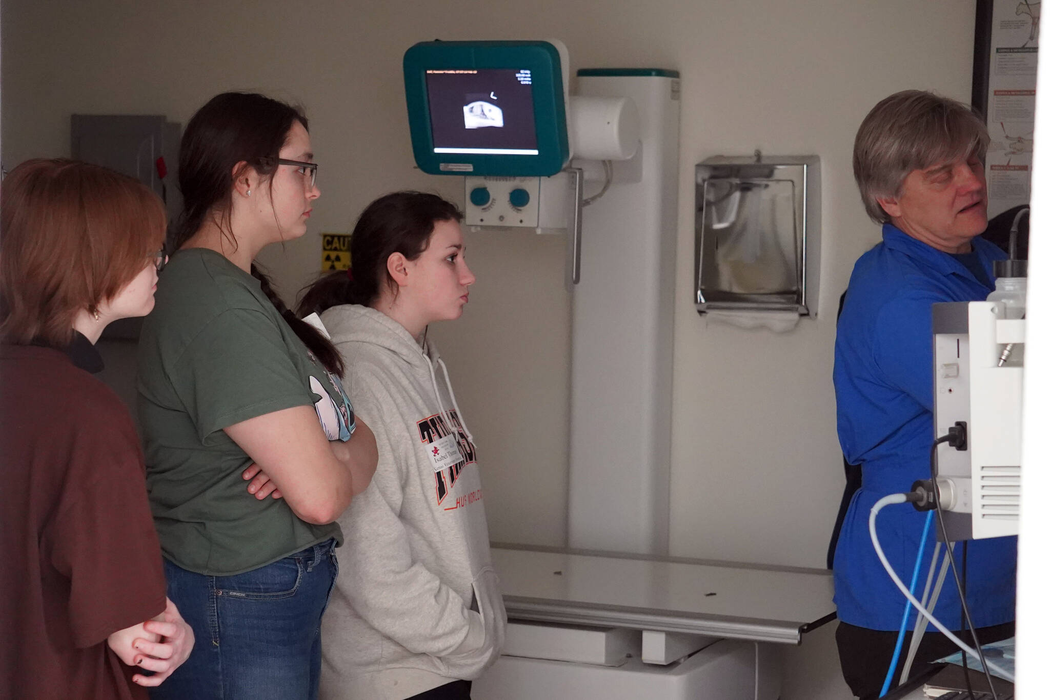 Jylann Green, Aaliyah Bookey and Isabel Thomas watch Dr. Curt Wisnewski as he shows off some x-rays at Kenai Veterinary Hospital in Kenai, Alaska, on Job Shadow Day, Tuesday, Feb. 13, 2024. (Michelle Duffield/Peninsula Clarion)