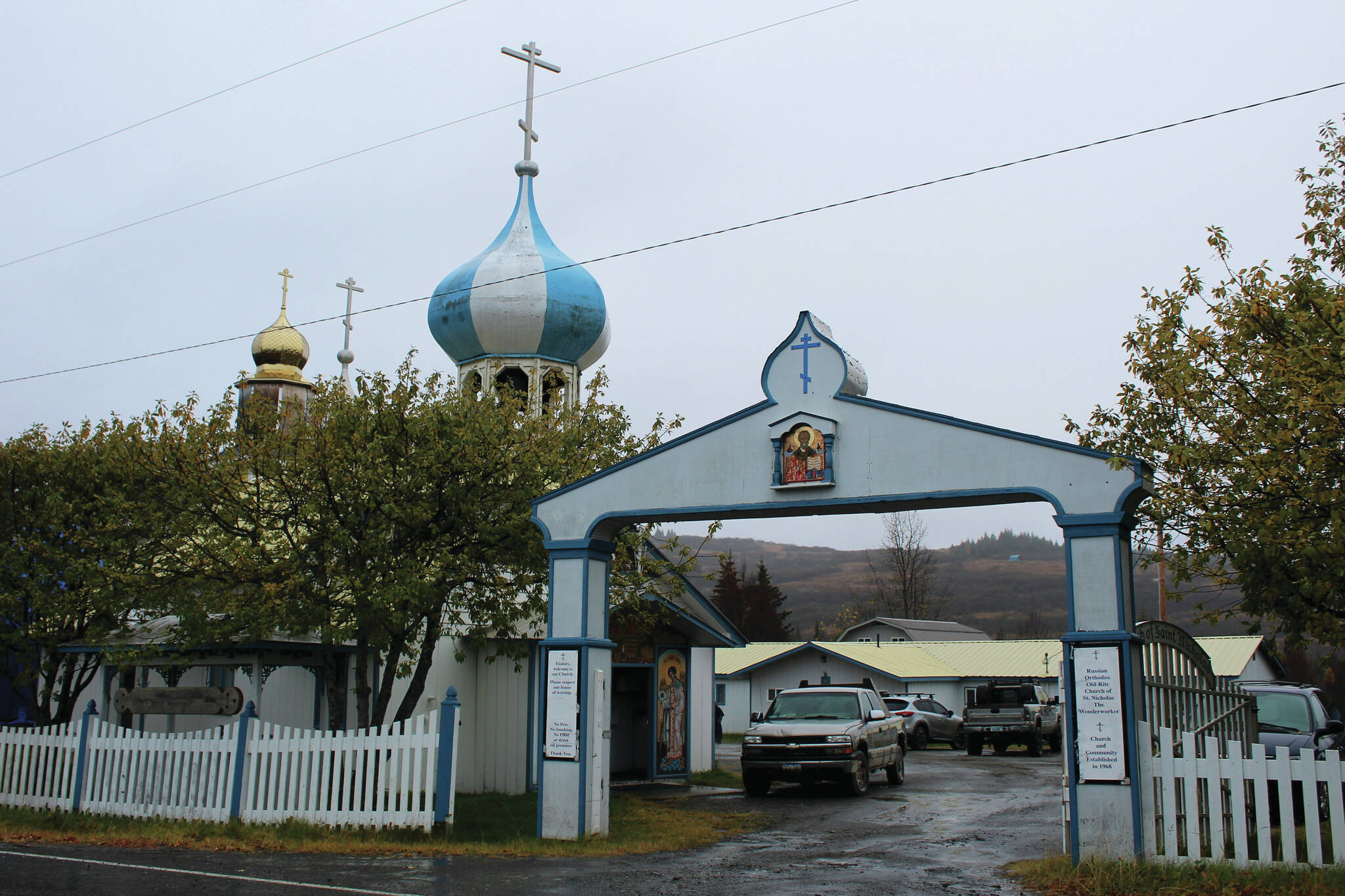 An arch marks the entrance to the Church of St. Nicholas on Tuesday, Oct. 10, 2023, in Nikolaevsk, Alaska. In rear, cars are parked in front of a building that has been used this school year as a makeshift classroom for families part of a home-school cooperative. (Ashlyn O’Hara/Peninsula Clarion)