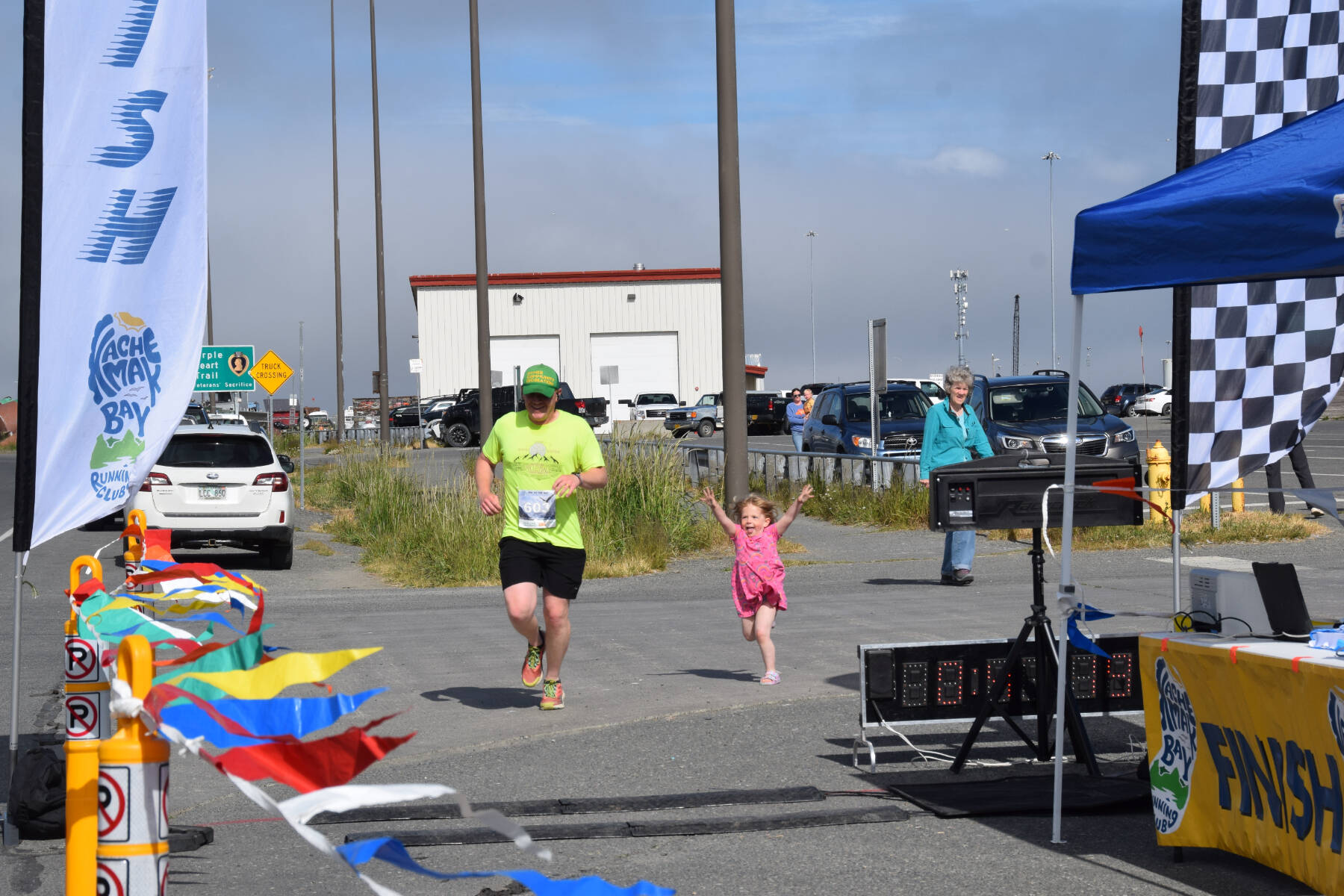 Daniel Newsted from Anchor Point crosses the finish line, accompanied by his daughter who caught up from the sidelines, during the Homer Spit Run Cosmic Hamlet Half Marathon on Saturday, June 29, 2024, in Homer, Alaska. (Delcenia Cosman/Homer News)