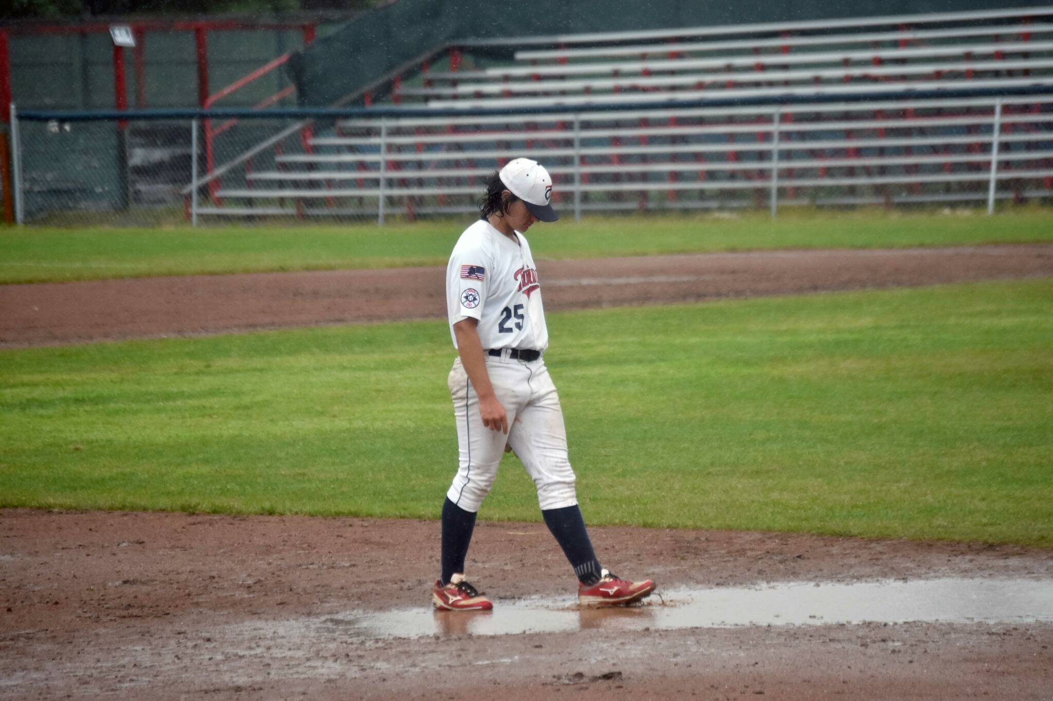 Post 20 Twins third baseman Gabe Smith explores the puddle at his position Saturday, July 6, 2024, at Coral Seymour Memorial Park in Kenai, Alaska. (Photo by Jeff Helminiak/Peninsula Clarion)
