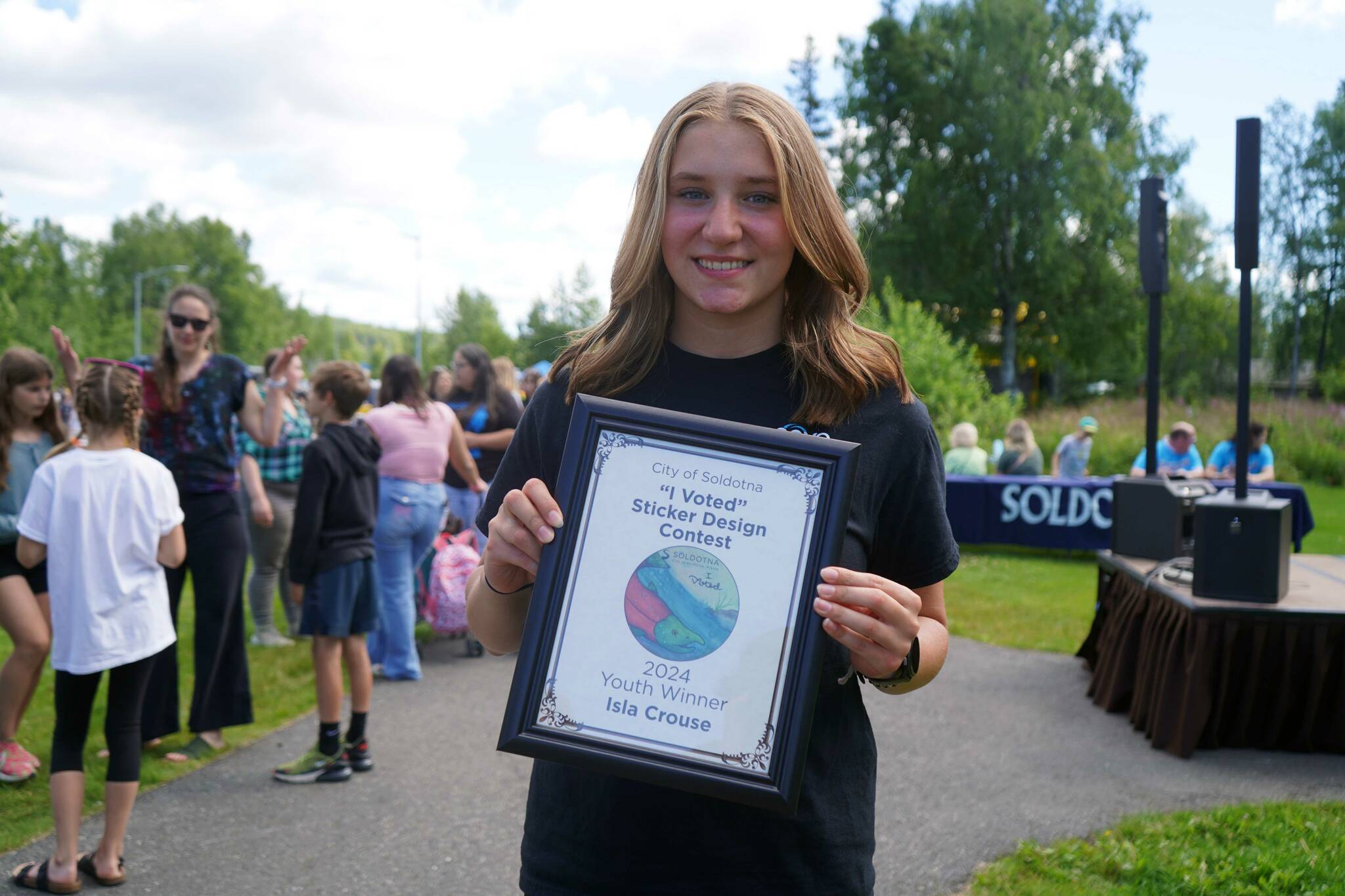 Isla Crouse stands with her award for winning the City of Soldotna’s “I Voted” Sticker Design Contest at the Soldotna Progress Days Block Party in Parker Park in Soldotna, Alaska, on Saturday, July 27, 2024. (Jake Dye/Peninsula Clarion)