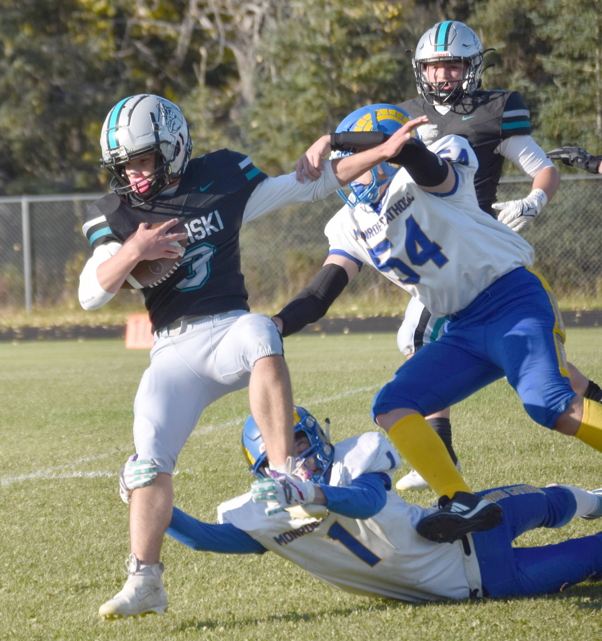 Nikiski’s Kaiden Parrish picks up yardage against Monroe Catholic’s Isaiah Snow and Taylor Pearson on Friday, Sept. 20, 2024, at Nikiski Middle-High School in Nikiski, Alaska. (Photo by Jeff Helminiak/Peninsula Clarion)