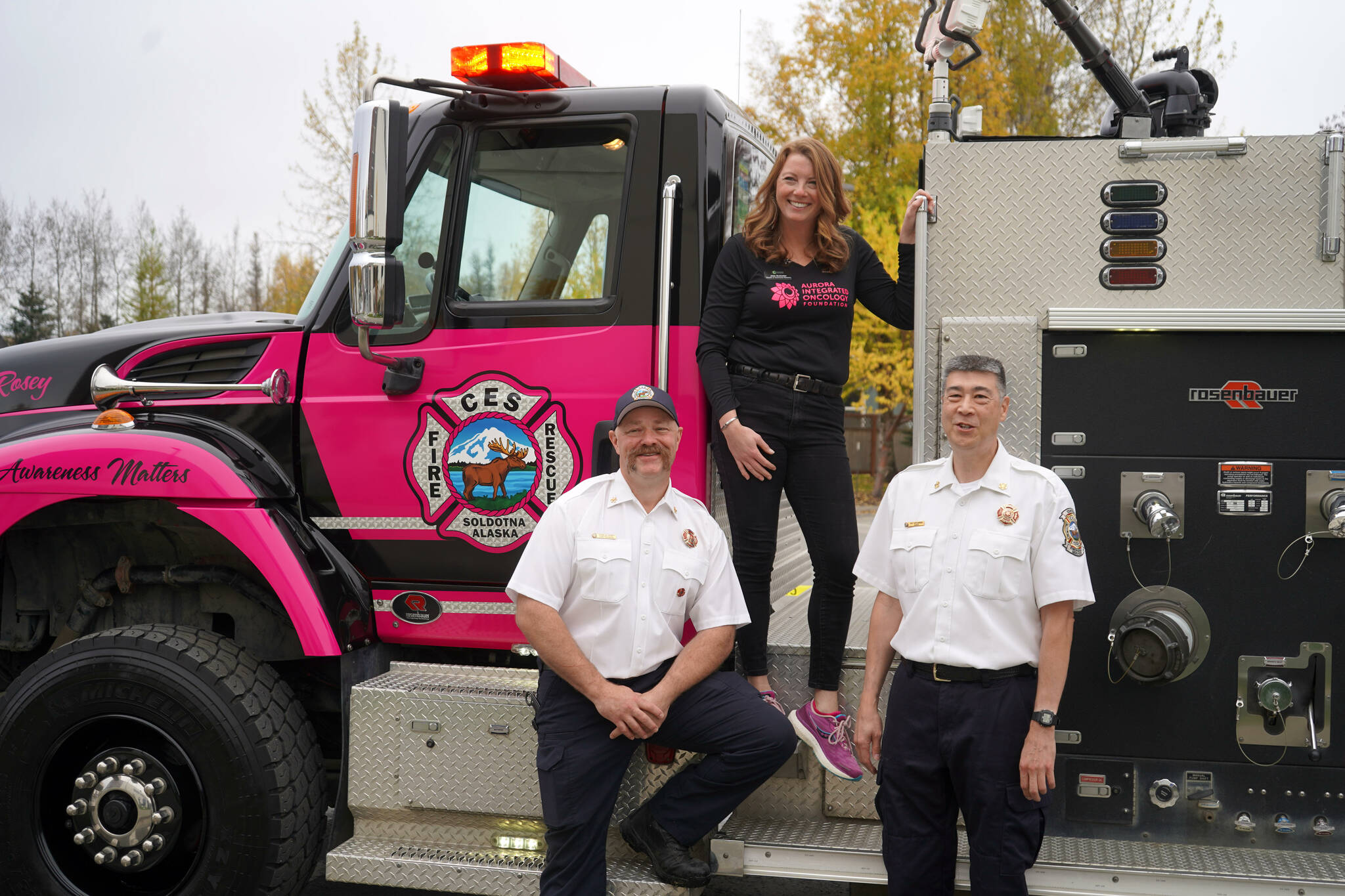 Jess Gutzwiler, director of community outreach for Aurora Integrated Oncology Foundation, stands with Central Emergency Services Fire Marshal Charles Roney and Chief Roy Browning during an unveiling of “Miss Rosey,” a pink fire engine dedicated to raising awareness about cancer prevention and screening, at Central Peninsula Hospital in Soldotna, Alaska, on Saturday, Sept. 28, 2024. (Jake Dye/Peninsula Clarion)