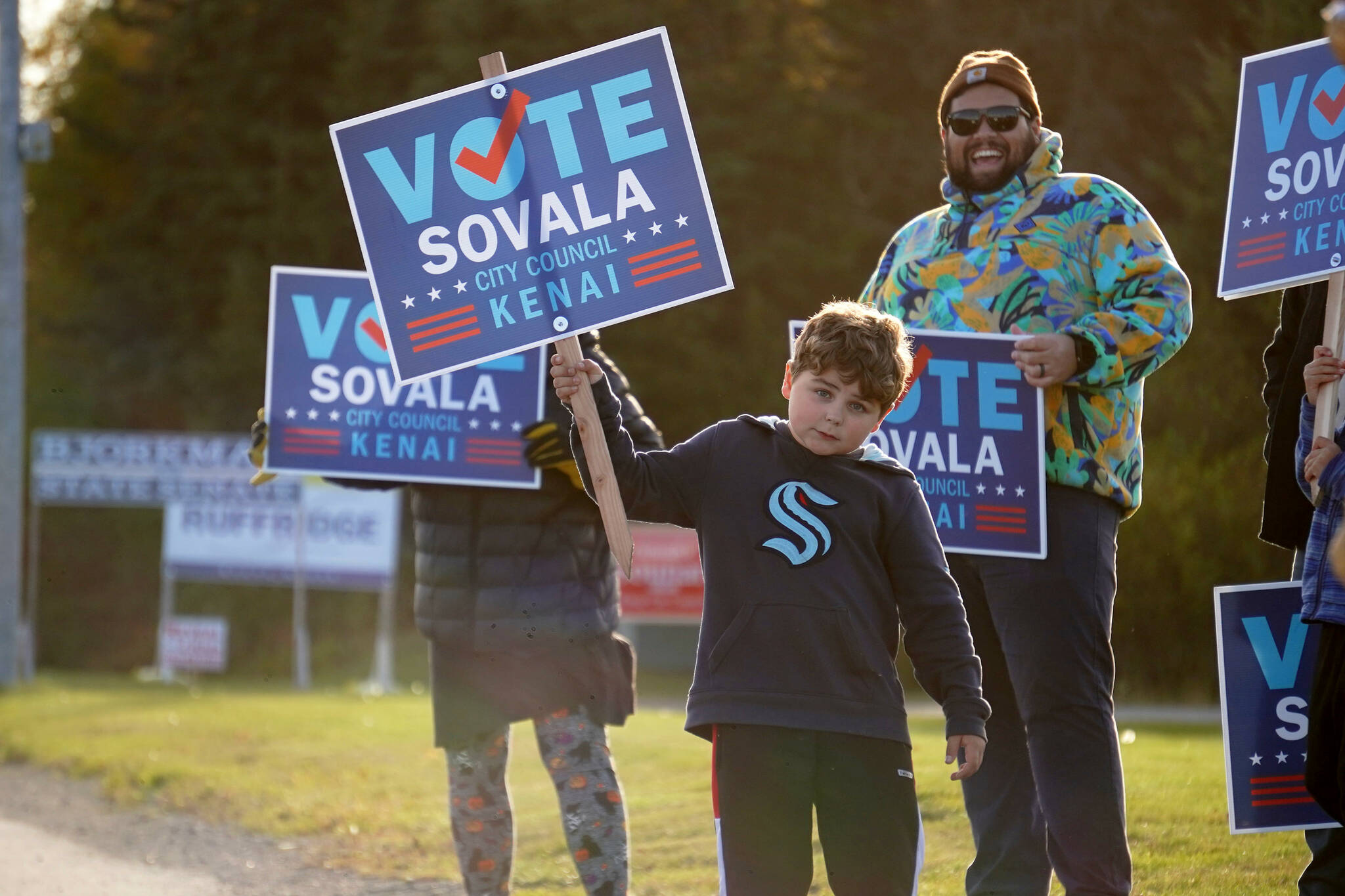 Supporters of Kenai City Council candidate Sovala Kisena wave signs at the side of the Kenai Spur Highway in Kenai, Alaska, on Tuesday, Oct. 1, 2024. (Jake Dye/Peninsula Clarion)