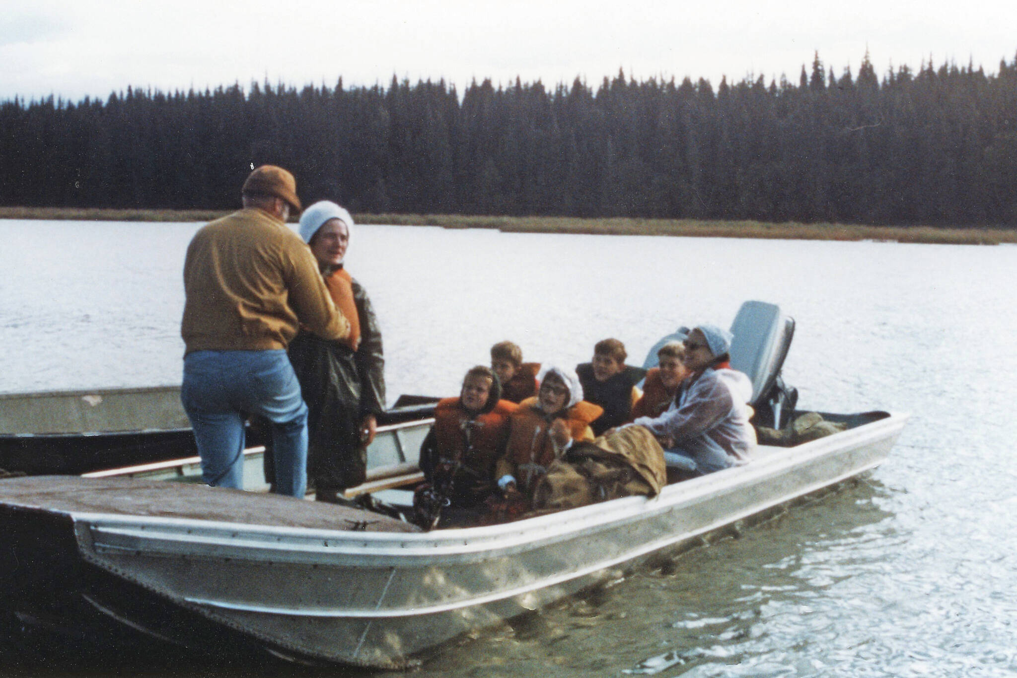 Jane Fair (standing, wearing white hat) receives help with her life jacket from Ron Hauswald prior to the Fair and Hauswald families embarking on an August 1970 cruise with Phil Ames on Tustumena Lake. Although conditions were favorable at first, the group soon encountered a storm that forced them ashore. (Photo courtesy of the Fair Family Collection)