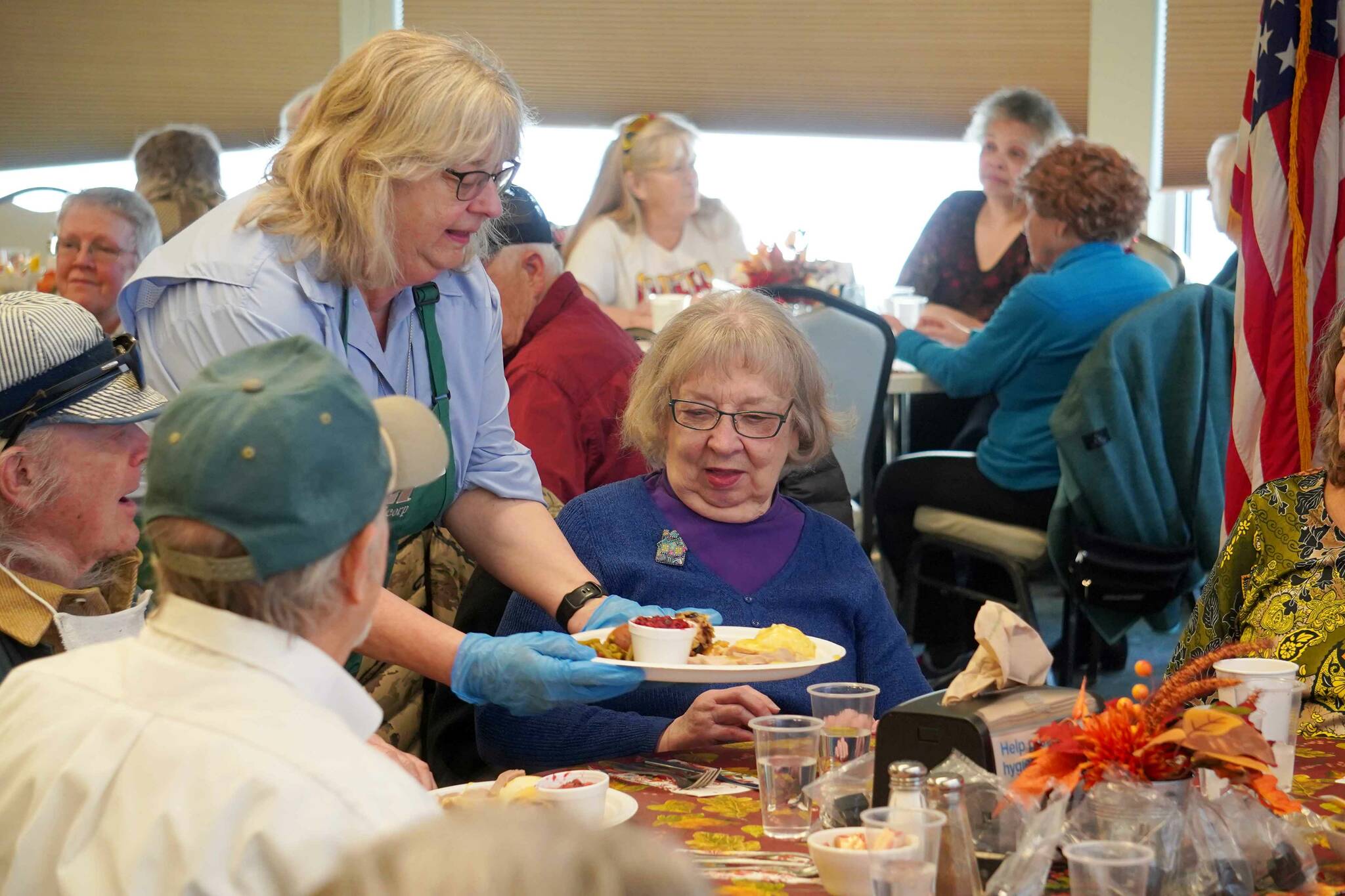 Kenai City Council member and Hilcorp volunteer Victoria Askin delivers a Thanksgiving meal to Ava Bassett during the Hilcorp Areawide Senior Thanksgiving Luncheon in the Kenai Senior Center banquet hall in Kenai, Alaska, on Friday, Nov. 22, 2024. (Jake Dye/Peninsula Clarion)