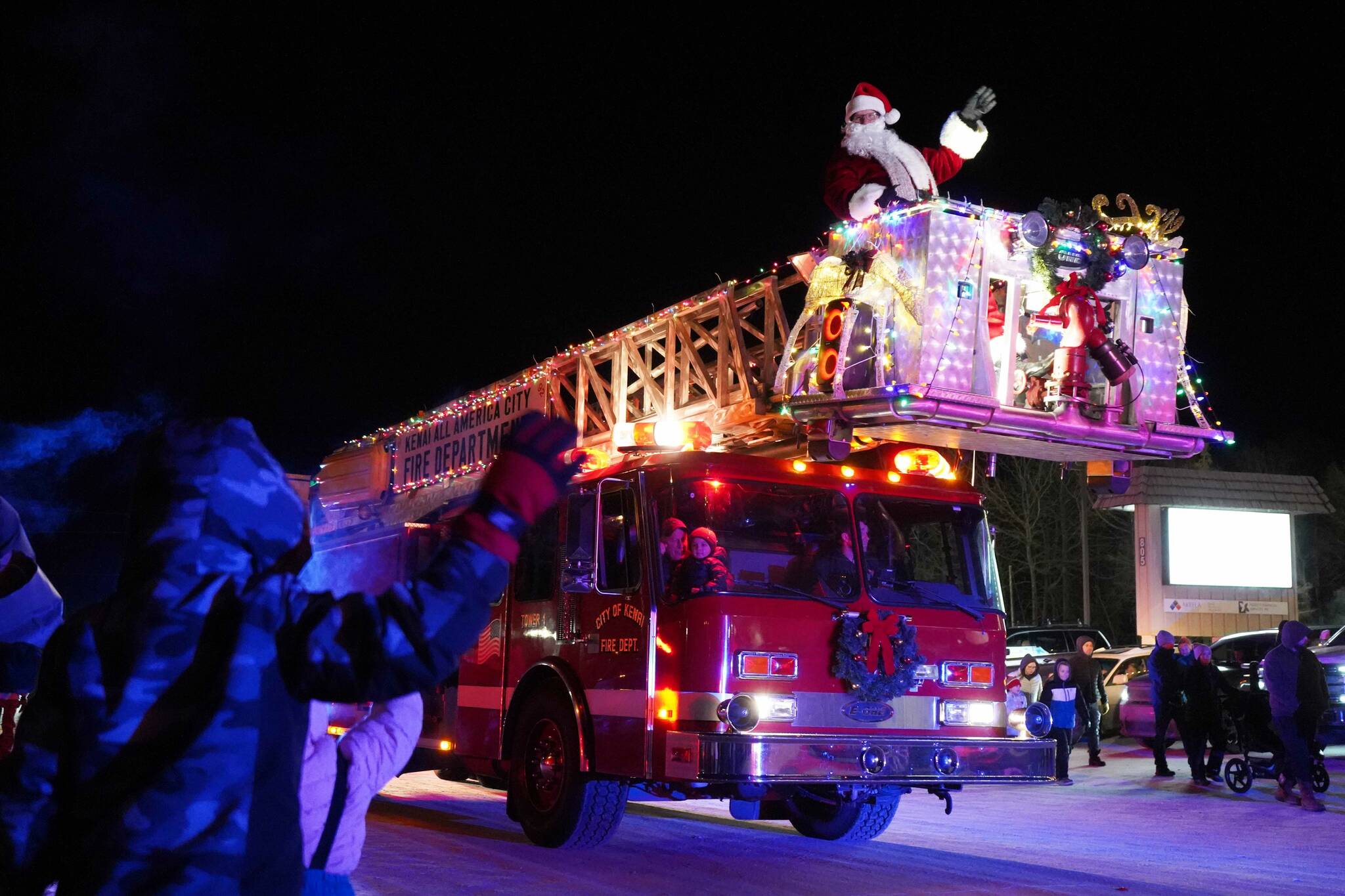 Santa Claus waves at children from atop a Kenai Fire Department engine on Frontage Street in Kenai, Alaska, as part of the Electric Lights Parade on Friday, Nov. 29, 2024. (Jake Dye/Peninsula Clarion)