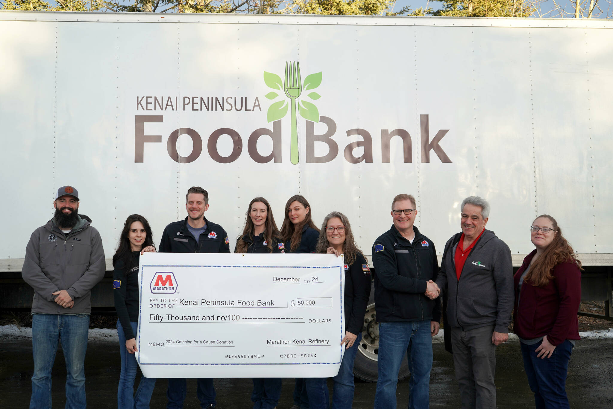 Marathon Petroleum Kenai Refinery General Manager Bruce Jackman presents a novelty check for $50,000 to the Kenai Peninsula Food Bank at the Kenai Peninsula Food Bank in Soldotna, Alaska, on Wednesday, Dec. 11, 2024. (Jake Dye/Peninsula Clarion)