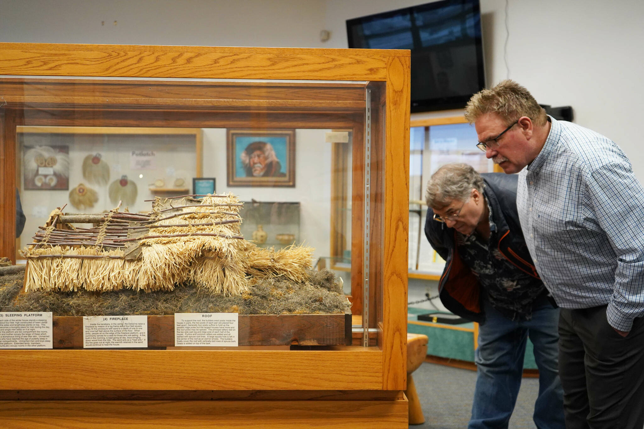 Marty Askin and Brian Gabriel inspect a displayed model of a traditional Dena’ina home called a nichil during the grand reopening of the cultural center at the Kenai Chamber of Commerce and Visitor Center in Kenai, Alaska, on Wednesday, Jan. 15, 2025. (Jake Dye/Peninsula Clarion)